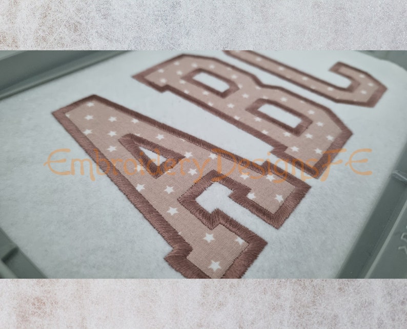 May include: Embroidered letters A, B, and C in a brown color with a white star pattern on a light blue fabric.