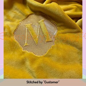 May include: A yellow plush blanket with a gold embroidered letter "M" in a decorative frame. Stitched by "Customer".