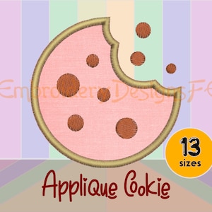 May include: A pink cookie with brown chocolate chips and a bite taken out of it. The cookie is outlined in gold and has a white background. The text "Applique Cookie" is written in red below the cookie. The text "13 sizes" is written in black on a yellow circle.