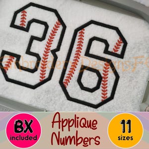 May include: An embroidery design featuring the number 36 in a block font. The numbers are white with a thick black outline and a red baseball stitch pattern running through the center. The design is displayed inside a grey embroidery hoop.