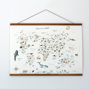 Könnte beinhalten: Eine dekorative Weltkarte mit Illustrationen von Tieren und Wahrzeichen. Die Karte wird von magnetischen Holz-Posterhaltern gehalten und vor einer weißen Wand präsentiert. Der deutsche Text "Unsere Welt" steht oben auf der Karte.