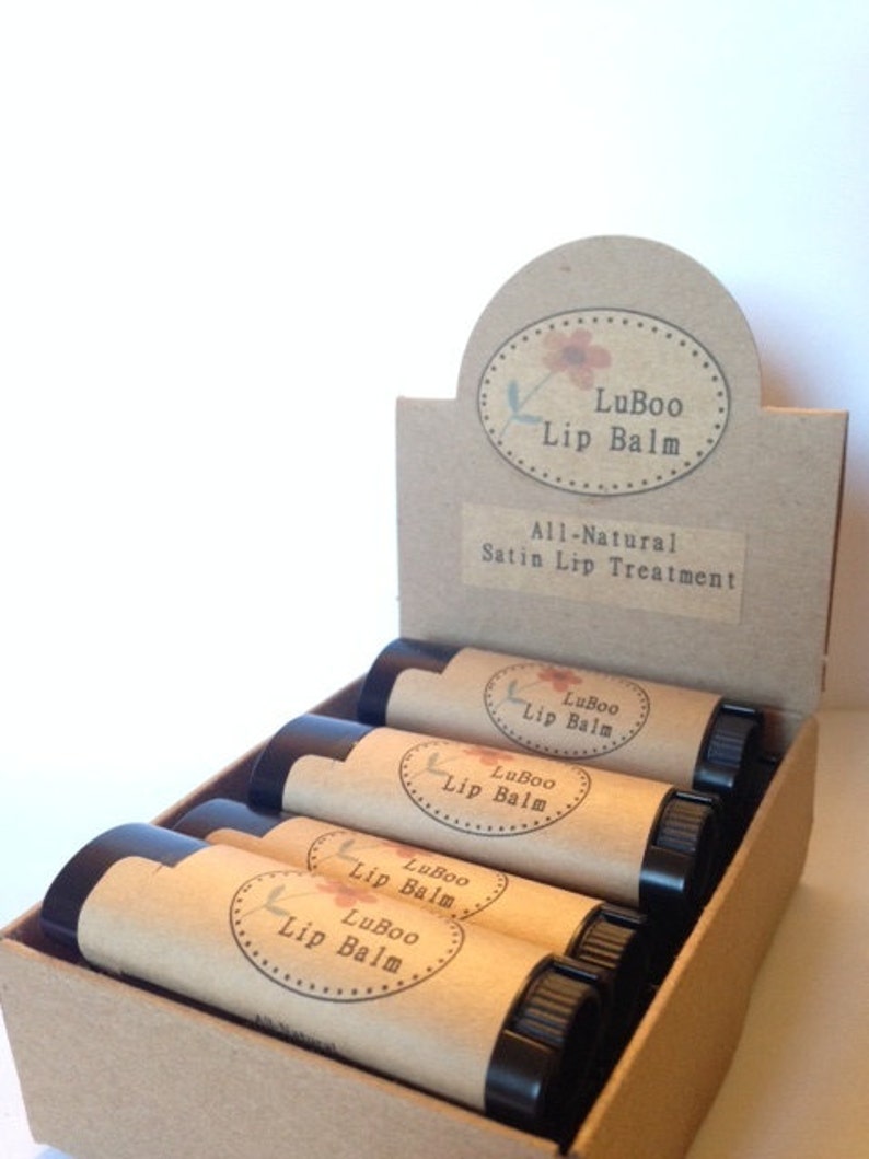 Puede incluir: Una caja de tubos de b&aacute;lsamo labial LuBoo. Los tubos son marrones con una etiqueta blanca que dice "LuBoo Lip Balm". La caja es marr&oacute;n y tiene una etiqueta que dice "LuBoo Lip Balm All-Natural Satin Lip Treatment".
