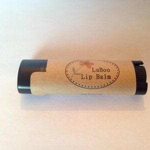 Puede incluir: Un tubo de b&aacute;lsamo labial marr&oacute;n y negro con una etiqueta que dice "LuBoo Lip Balm" y un peque&ntilde;o dise&ntilde;o de flor.
