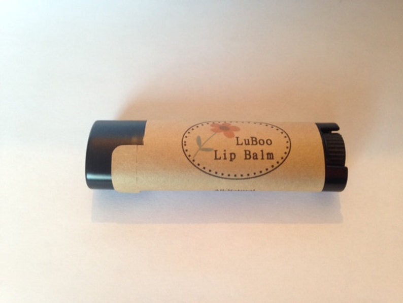 Puede incluir: Un tubo de b&aacute;lsamo labial marr&oacute;n y negro con una etiqueta que dice "LuBoo Lip Balm" y un peque&ntilde;o dise&ntilde;o de flor.