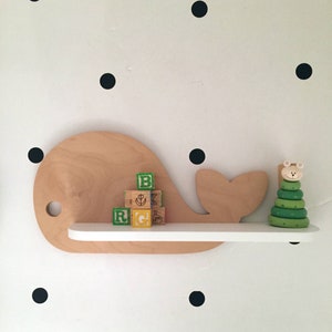 May include: A wooden whale-shaped shelf with a white shelf and a green and white stacking toy. The shelf is mounted on a white wall with black polka dots.