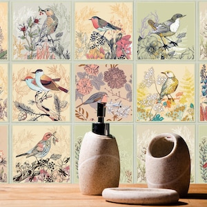 May include: A set of square wall tiles featuring various bird and botanical illustrations in muted tones, displayed behind a beige soap dispenser, a matching toothbrush holder, and a soap dish on a wooden surface.
