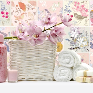May include: A white wicker basket filled with pink orchids, a pink bottle of bath salts, a pink candle, and white towels. The background is a pink and white tiled wall with a floral pattern.