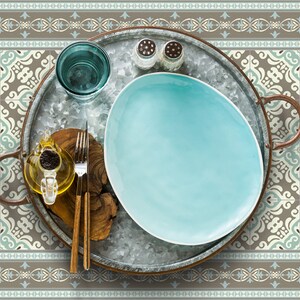May include: A metal serving tray with a blue ceramic plate, a glass of water, a small bottle of oil, and two salt and pepper shakers. The tray is set on a brown and blue patterned placemat.