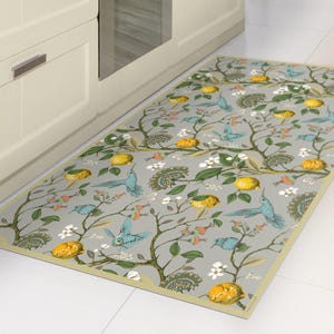 May include: Rectangular kitchen mat with a gray background featuring a botanical design. The pattern includes blue birds, yellow lemons, green leaves, and white flowers. The mat is placed in front of a white cabinet.