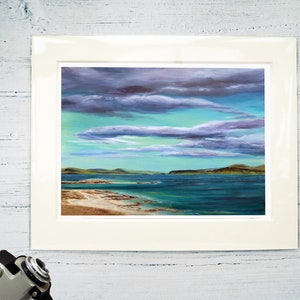 May include: A framed painting of a seascape with a sandy beach, turquoise water, and a cloudy sky. The clouds are a mix of purple and gray, and the water is a deep blue.