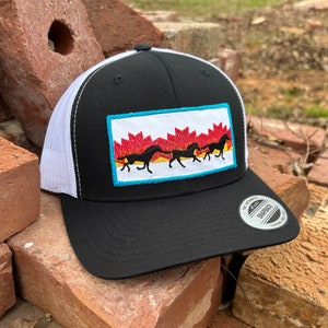 May include: Black and white trucker hat with a white mesh back. The hat features a colourful embroidered patch of five horses running across a red and orange background. The patch has a turquoise border.