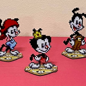 Puede incluir: Tres figuras de personajes de dibujos animados de la serie animada "Animaniacs". Los personajes son Yakko, Wakko y Dot. Cada figura está de pie sobre una base con el logotipo del programa.