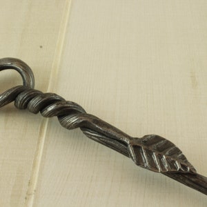 Op de afbeelding: Een handgesmeed ijzeren haardbezem met een gedraaide handgreep en een bladvormig uiteinde.