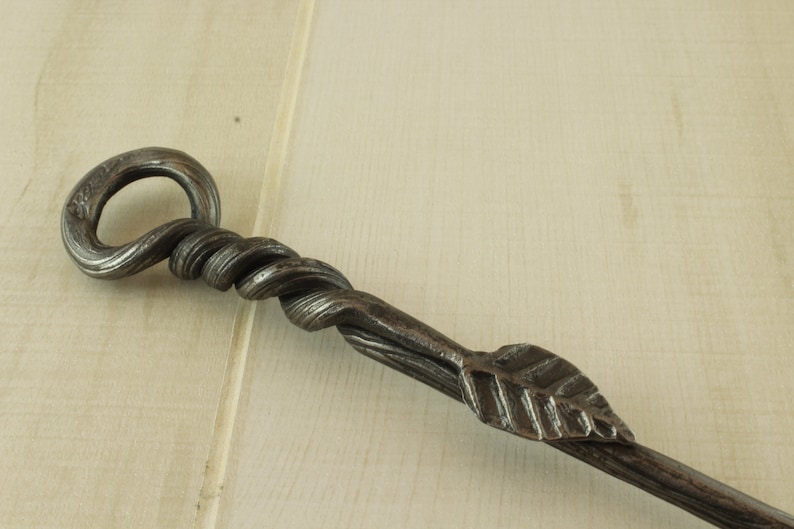 Op de afbeelding: Een handgesmeed ijzeren haardbezem met een gedraaide handgreep en een bladvormig uiteinde.