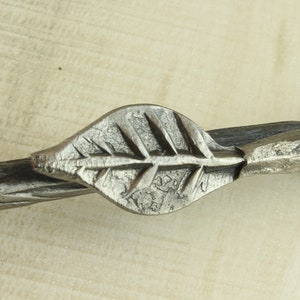 Op de afbeelding: Een zilveren metalen handvat in de vorm van een blad met een gedraaide metalen steel.