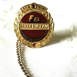 May include: Gold-colored pin with a red and gold emblem that reads "For 5 Years FB Farm Bureau Service to Agriculture". The pin has a gold chain and a gold bar.