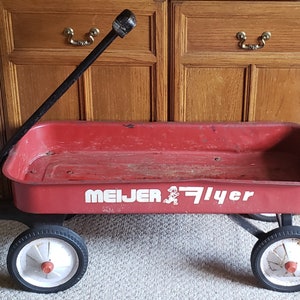 May include: A red wagon with a black handle and white wheels. The wagon has the words 