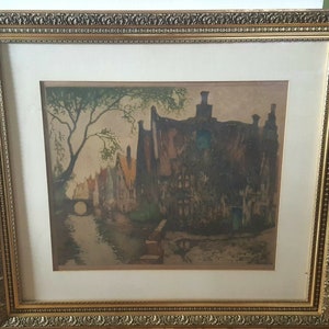 May include: A framed print of a watercolor painting depicting a canal scene with buildings and a bridge. The buildings are painted in shades of brown and gray, and the water is a light blue. The print is framed in a gold frame.