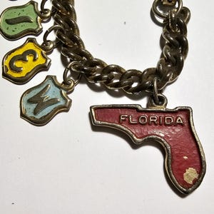 May include: A gold chain charm bracelet with multiple charms, including a red and gold charm shaped like the state of Florida with the word "FLORIDA" written on it.