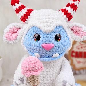 Pu&ograve; includere: Un giocattolo di peluche all'uncinetto blu e bianco con corna rosse e bianche, che tiene un cono gelato rosa all'uncinetto. Il giocattolo ha grandi occhi neri con accenti arcobaleno.