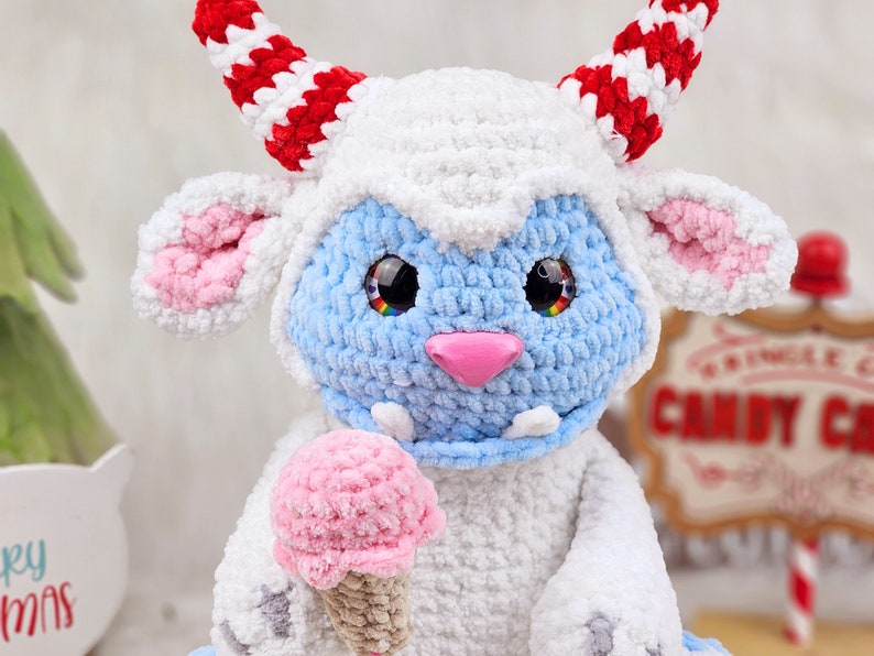 Pu&ograve; includere: Un giocattolo di peluche all'uncinetto blu e bianco con corna rosse e bianche, che tiene un cono gelato rosa all'uncinetto. Il giocattolo ha grandi occhi neri con accenti arcobaleno.