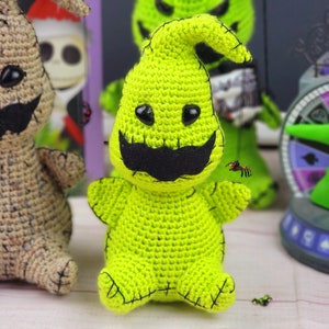 Puede incluir: Un juguete de peluche verde tejido a crochet del personaje Oogie Boogie de la pel&iacute;cula Pesadilla antes de Navidad. El juguete tiene una boca cosida negra, ojos negros y un bigote cosido negro. El juguete est&aacute; sentado sobre una superficie blanca.