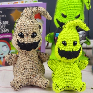Puede incluir: Dos personajes de Pesadilla Antes de Navidad hechos a crochet, uno verde y otro marr&oacute;n, con ojos negros y un bigote negro. Los personajes est&aacute;n sentados sobre una superficie blanca.