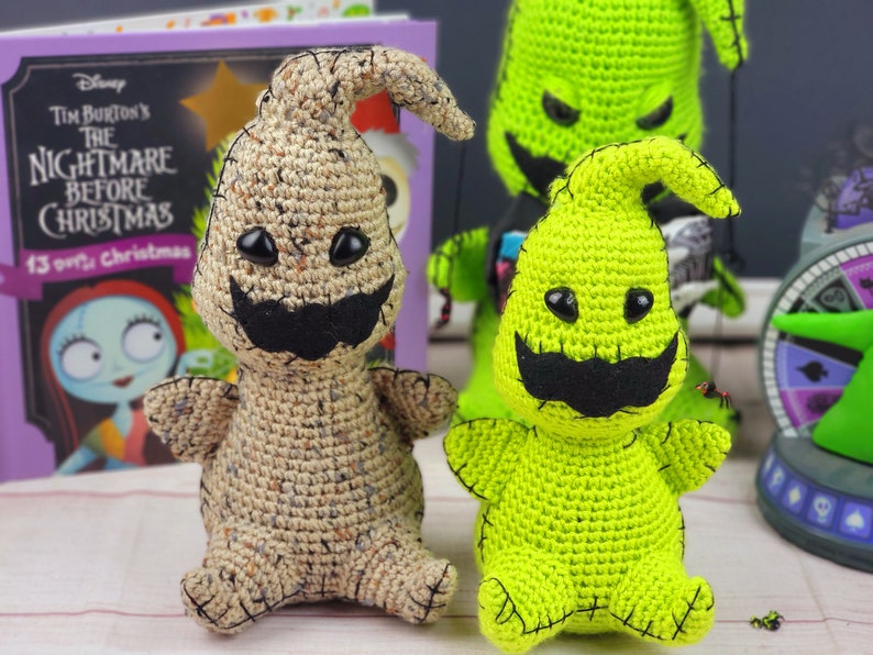 Puede incluir: Dos personajes de Pesadilla Antes de Navidad hechos a crochet, uno verde y otro marr&oacute;n, con ojos negros y un bigote negro. Los personajes est&aacute;n sentados sobre una superficie blanca.