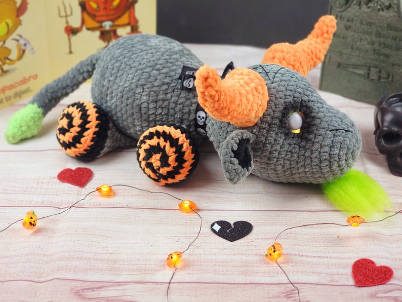 Peut inclure: Un dragon en crochet gris fait &agrave; la main avec des cornes et des accents orange, des roues noires et orange et une langue verte. Le dragon a une &eacute;tiquette de cr&acirc;ne et est d&eacute;cor&eacute; de lumi&egrave;res et de coeurs sur le th&egrave;me d'Halloween.