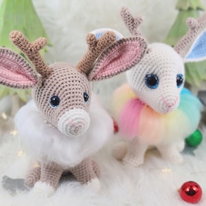 Könnte beinhalten: Zwei gehäkelte Rentierpuppen mit großen blauen Augen und flauschigen weißen Kragen. Eines ist hellbraun mit rosa gefütterten Ohren, das andere ist weiß mit blau gefütterten Ohren und einer regenbogenfarbenen, flauschigen Mähne. Weihnachtsdekoration.