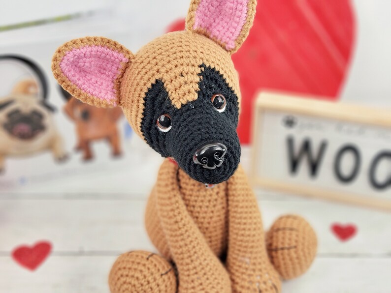 May include: A crocheted brown and black dog with pink ears. The dog is sitting with its front paws tucked in and its back paws extended.