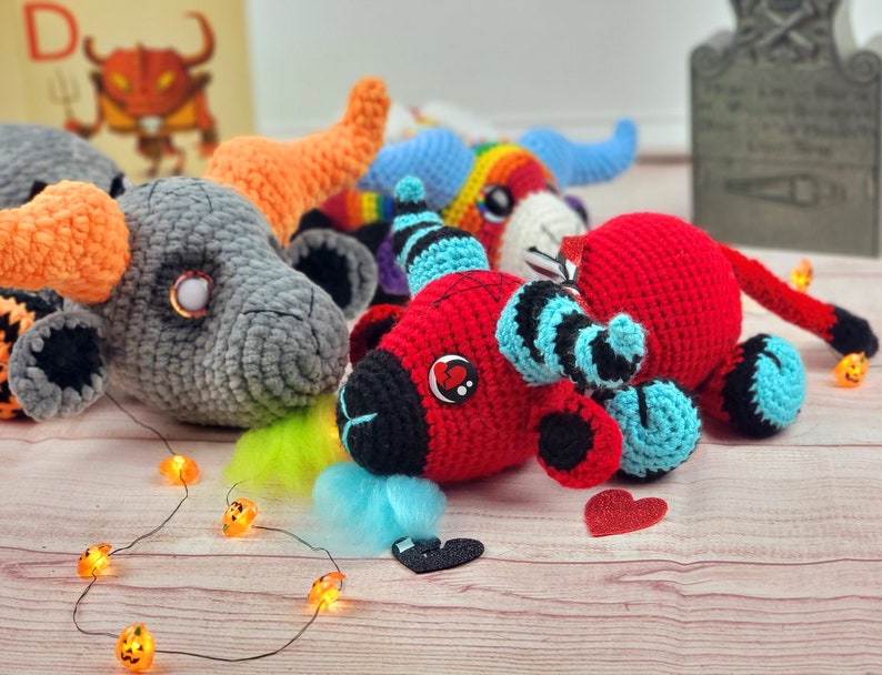 Peut inclure: Plusieurs peluches de taureaux crochet&eacute;es &agrave; la main, de couleurs vari&eacute;es, dont rouge, gris et arc-en-ciel. Chaque peluche a des cornes, des yeux et une queue. Des guirlandes lumineuses d'Halloween et des confettis en forme de c&oelig;ur sont dispers&eacute;s.