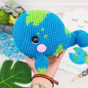 K&ouml;nnte beinhalten: Ein geh&auml;keltes Pl&uuml;schwalspielzeug mit einem blauen und gr&uuml;nen Farbschema, das die Erde darstellt. Der Wal hat eine rosa Nase und schwarze Augen.