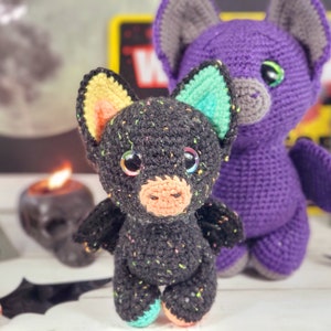 May include: Two crocheted bat toys. One is black with colorful accents and the other is purple. Both have large eyes and wings.