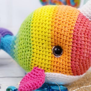 K&ouml;nnte beinhalten: Ein regenbogenfarbenes, geh&auml;keltes Narwal-Pl&uuml;schtier mit einem wei&szlig;en Horn und einem schwarzen Auge. Das Spielzeug ist aus verschiedenen Farben gefertigt, darunter Lila, Blau, Gr&uuml;n, Gelb, Orange und Rot.