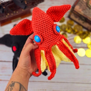 May include: A crocheted red and yellow octopus with blue eyes. The octopus is being held by a hand.