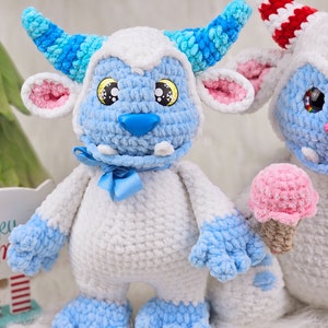 Pu&ograve; includere: Due giocattoli di peluche all'uncinetto a forma di mostri blu e bianchi. Il mostro a sinistra ha un corno a strisce blu e bianche e un fiocco blu. Il mostro a destra tiene un cono gelato rosa all'uncinetto.