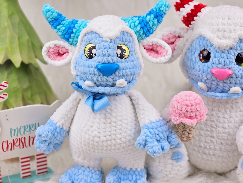 Pu&ograve; includere: Due giocattoli di peluche all'uncinetto a forma di mostri blu e bianchi. Il mostro a sinistra ha un corno a strisce blu e bianche e un fiocco blu. Il mostro a destra tiene un cono gelato rosa all'uncinetto.