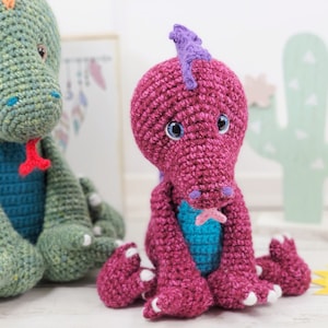 May include: Two handmade crochet dragon toys. One is green with a blue belly and red tongue, the other is magenta with a turquoise belly and purple accents. Both have large, expressive eyes and white claws.