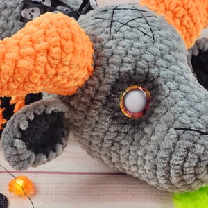 Peut inclure: Un monstre en peluche gris fait &agrave; la main avec des cornes orange et un pentagramme noir cousu sur la t&ecirc;te. Le monstre a un grand &oelig;il rond et une touffe de cheveux verts. Un ruban noir et blanc avec des t&ecirc;tes de mort est nou&eacute; autour du cou. Th&egrave;me d'Halloween.