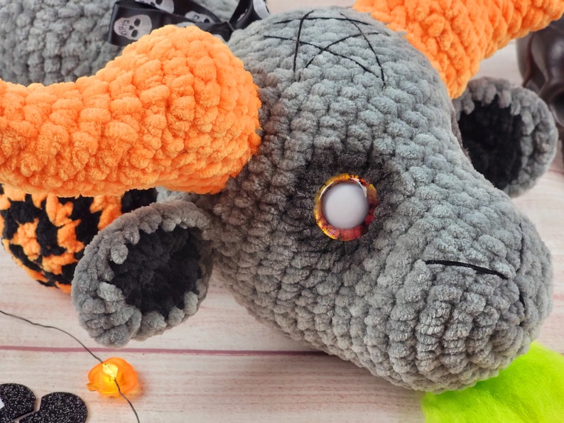 Peut inclure: Un monstre en peluche gris fait &agrave; la main avec des cornes orange et un pentagramme noir cousu sur la t&ecirc;te. Le monstre a un grand &oelig;il rond et une touffe de cheveux verts. Un ruban noir et blanc avec des t&ecirc;tes de mort est nou&eacute; autour du cou. Th&egrave;me d'Halloween.