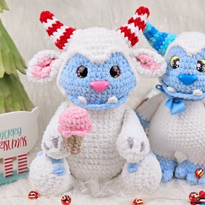 Pu&ograve; includere: Due giocattoli di peluche in crochet bianco con dettagli blu. Un giocattolo ha corna a strisce rosse e bianche e tiene un cono gelato rosa. L'altro giocattolo ha un fiocco blu ed &egrave; seduto accanto al primo giocattolo. I giocattoli sono seduti su una superficie bianca con decorazioni natalizie rosse e bianche.