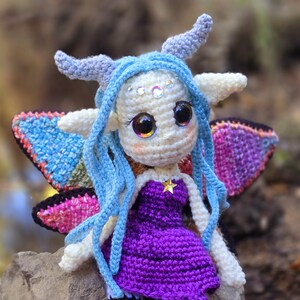 May include: A crocheted fairy doll with blue hair, purple dress, and iridescent wings. The doll has large eyes and a star on its chest.