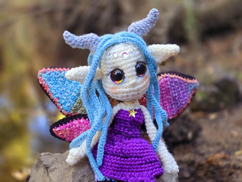 May include: A crocheted fairy doll with blue hair, purple dress, and iridescent wings. The doll has large eyes and a star on its chest.