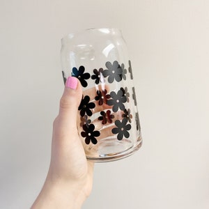 May include: A clear glass drinking glass with black flower designs. The glass is shaped like a can.