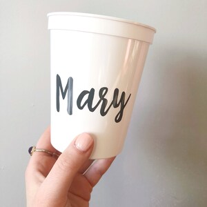 May include: White plastic cup with the name "Mary" written in black cursive lettering.
