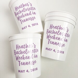 May include: Three white plastic cups with purple text that reads "Heather's Bachelorette Weekend in Tennessee May 4, 2018".