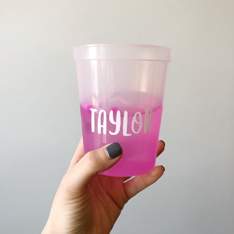 May include: A clear plastic cup with a pink liquid and the name "Taylor" written in white on the side.