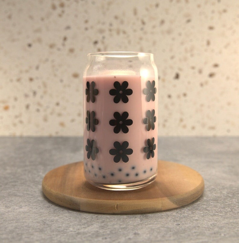 May include: A glass with a pink drink and black flower designs. The drink has small black tapioca balls.