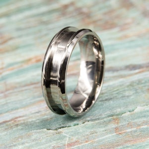 May include: A silver wedding band with a black inlay and a beveled edge.